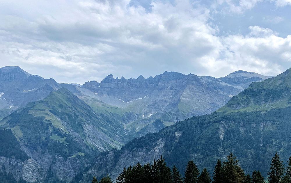 Blue-tinted mountains fill the whole lower half of the photo, with a cloudy sky above. The furthest mountains visible are quite craggy.