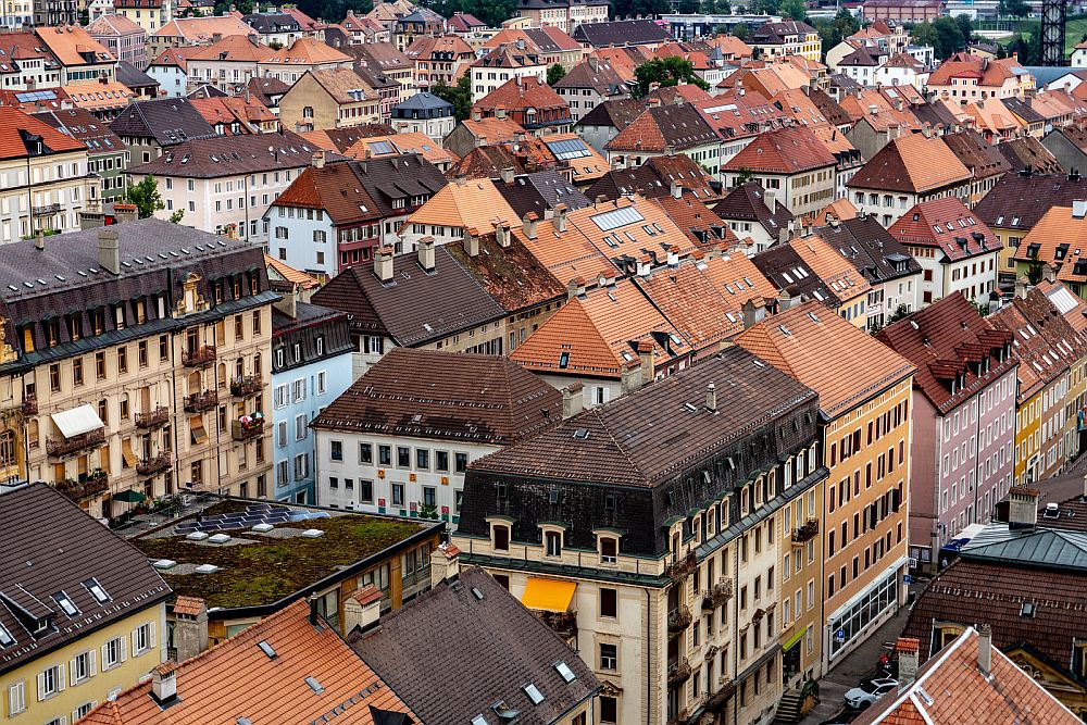 Buildings seen from above and to the side, in neat rows, mostly with red roofs and facads in shades of white and pastels. 