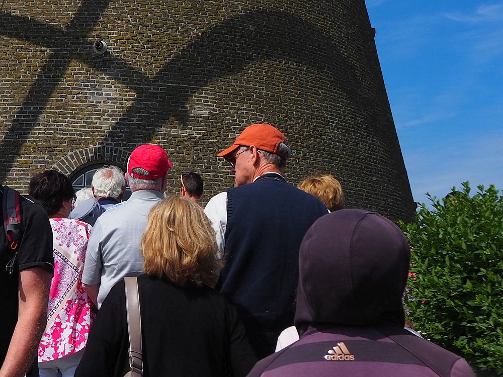 The backs of a group of tourists, with the brick wall of the windmill beyond them.