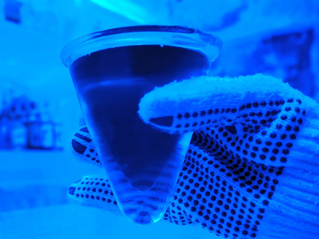 The photo, all very blue, is a closeup of my hand, gloved, holding a an ice glass with a dark liquid in it. The class is an upside-down cone shape.