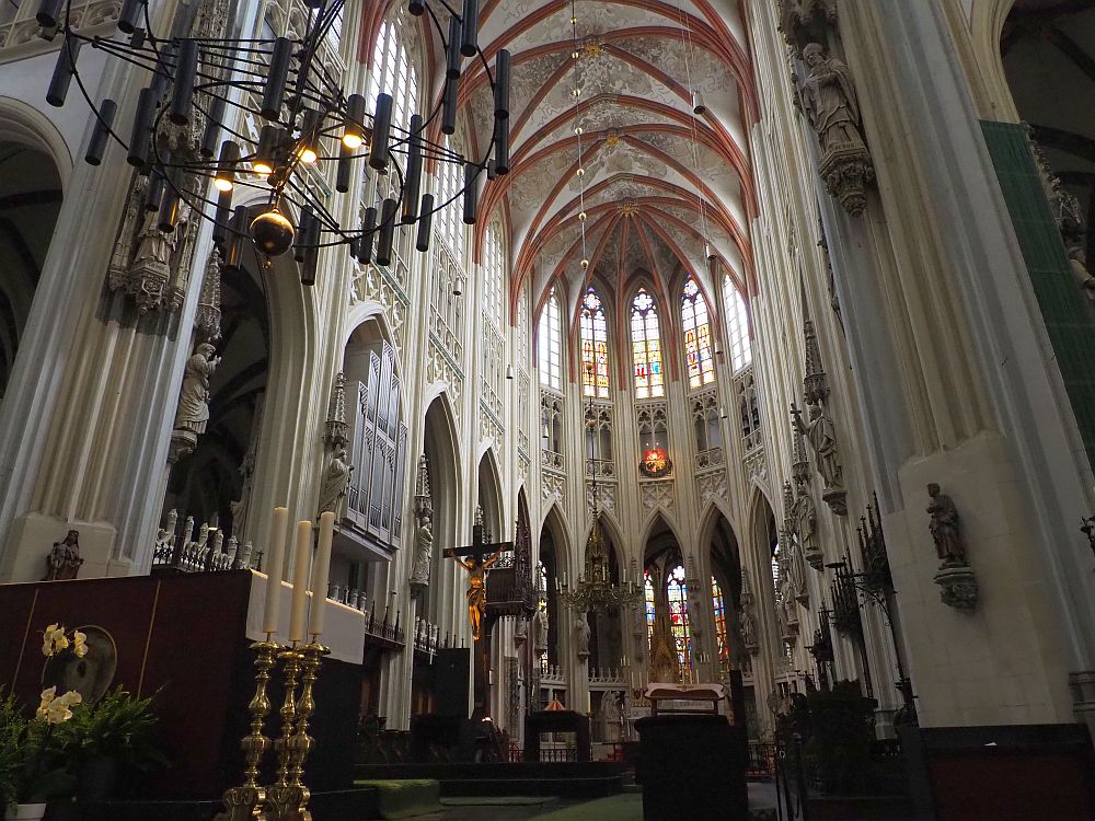 A very high-ceilings space with gothic arches all around it and stained glass between the arches. The ceiling is painted and every pillar betwen the arches has a sculpture of a saint on it. 