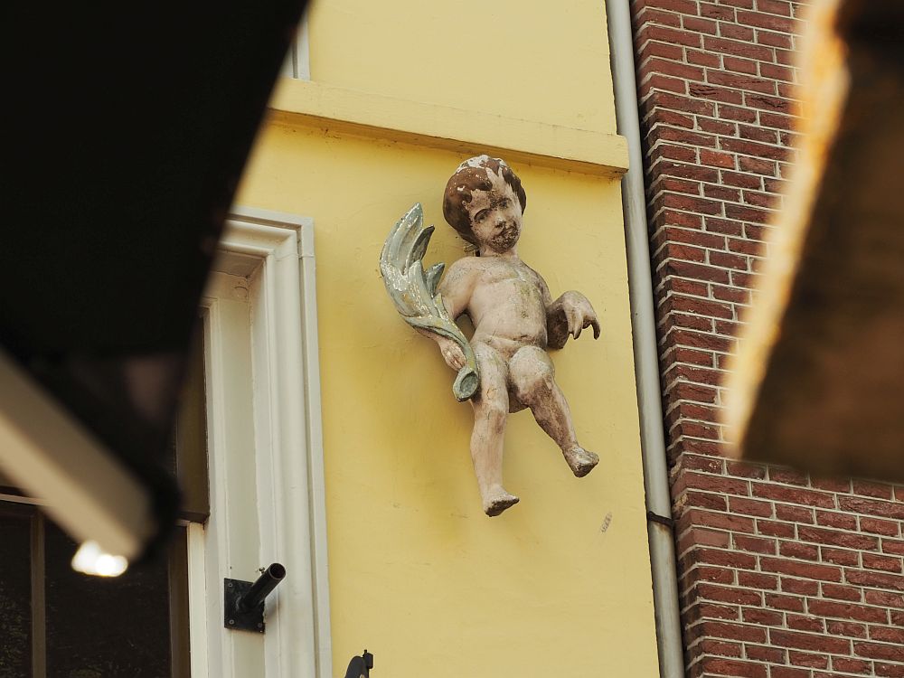 Seen looking upwards from below two cafe umbrellas, which frame the picture, a figure of a small naked child, like a cherub, but only one wing is visible on the left, and it looks like the child is holding it in his hand.