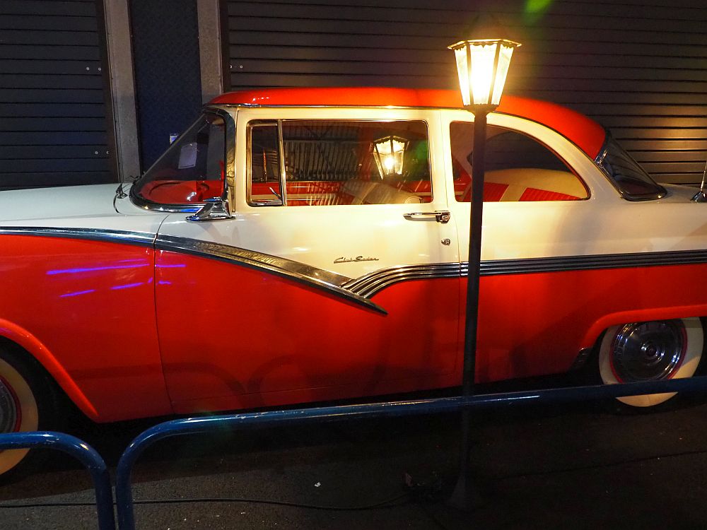 A 50's-style car, painted red and white, with what looks like a street light shining in front of it.