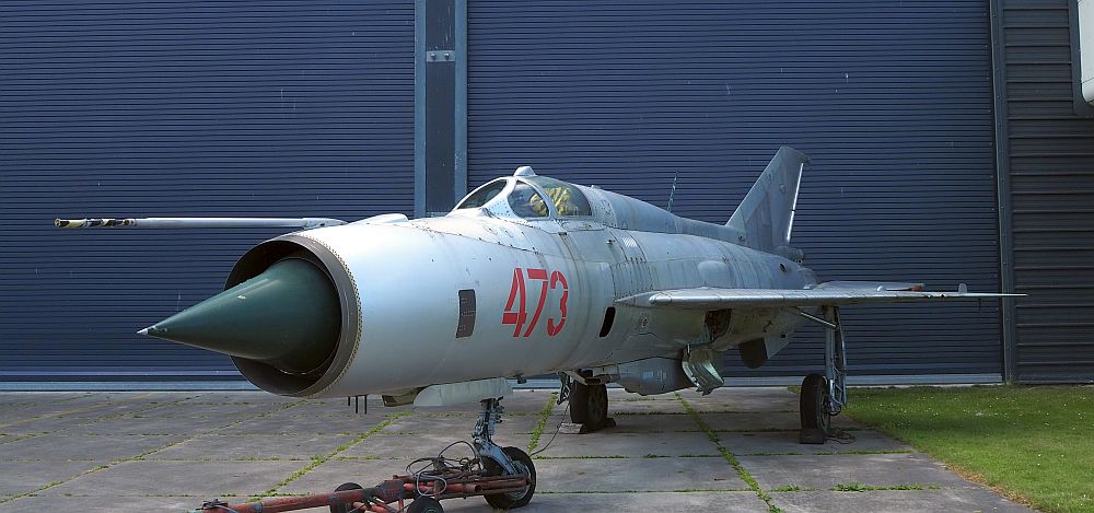 A small grey airplane with a glass covered cockpit that looks like it probably only fit one person. The front of the plane is very pointy and the wings don't extend very far out to the side, they reach back more than out.