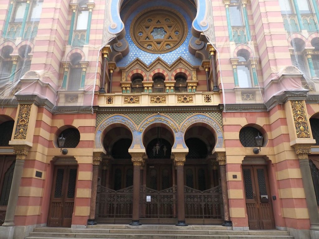 The entrance is in "moorish" style. The entrance has three rounded arches over the doorway, quite intricately painted, on pillars. Above that is a small decorative balcony, and over that is a large round window (stained glass perhaps) with a Jewish star in its center. Around that has a painted blue pattern.
