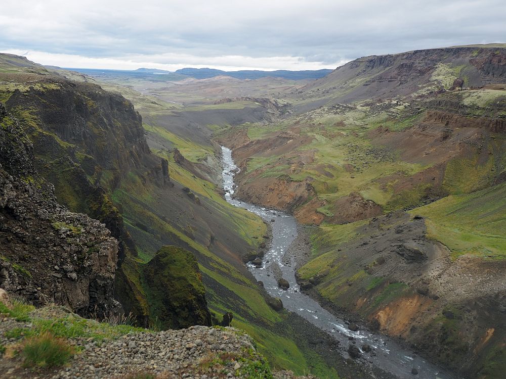 Looking down a long canyon that is less steep further on. Green hills on either side, the water in the river curves as it rounds the hills. Lots more hills in the background to the horizon.