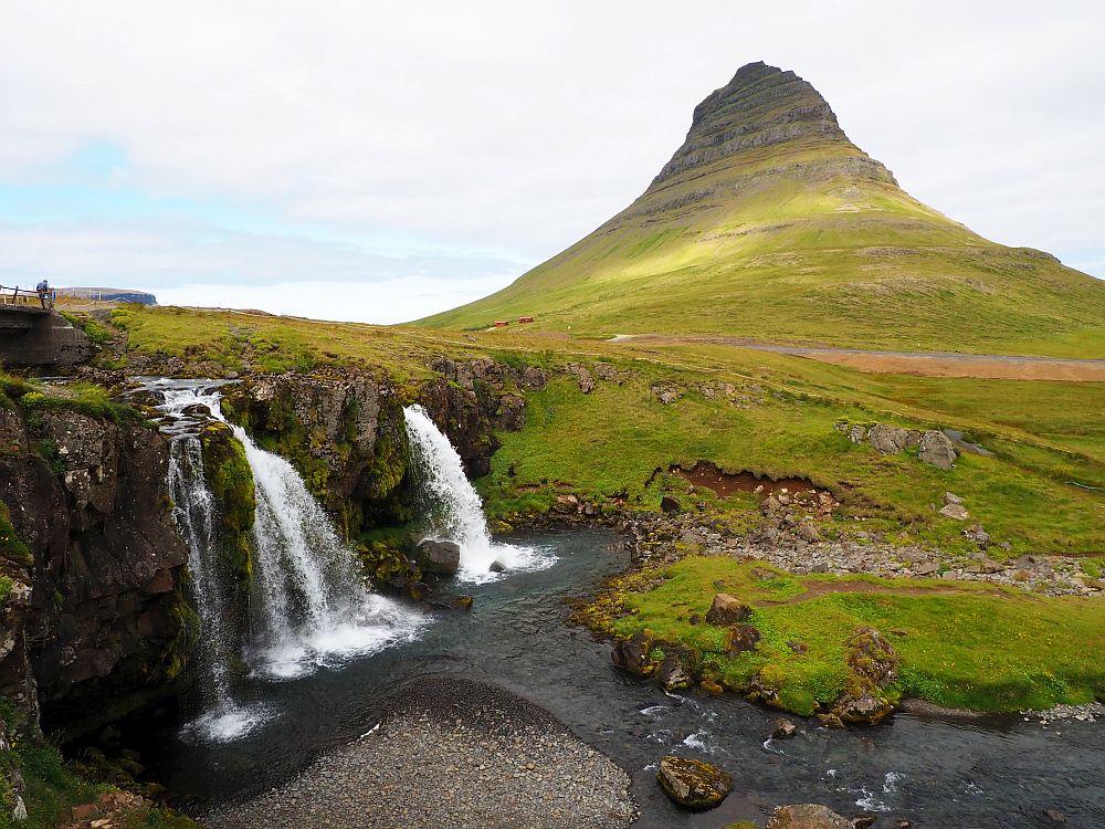 The waterfall descends at the left, split into several sections. Behind and to the right is a conical mountain.