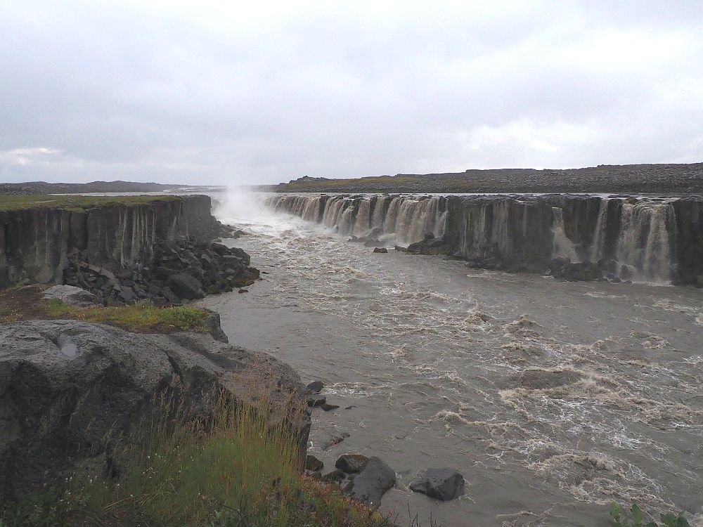 Looking up the river, a series of waterfalls line the opposite bank, made up of a long cliff. 