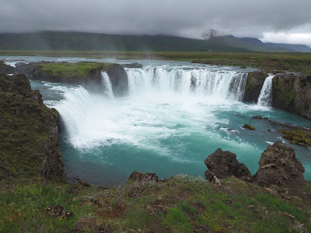 A classic crescent-shaped waterfall, actually several separate streams falling off the same shelf. The round pool below is blue, other than where the falls hit, where it's white. The blue is quite bright considering that it is a cloudy day.