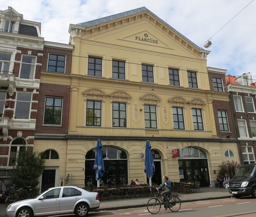 The building is quite grand: three stories, with the ground floor having arched doorways. The top is a triangle with the word "Plancius" and a small star of David.