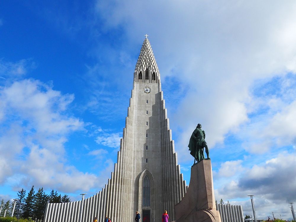 Hallgrimskirkja is made of concrete, with a triangular steeple made of vertical elements of increasing height. In front of it is a statue of Leif Ericson.