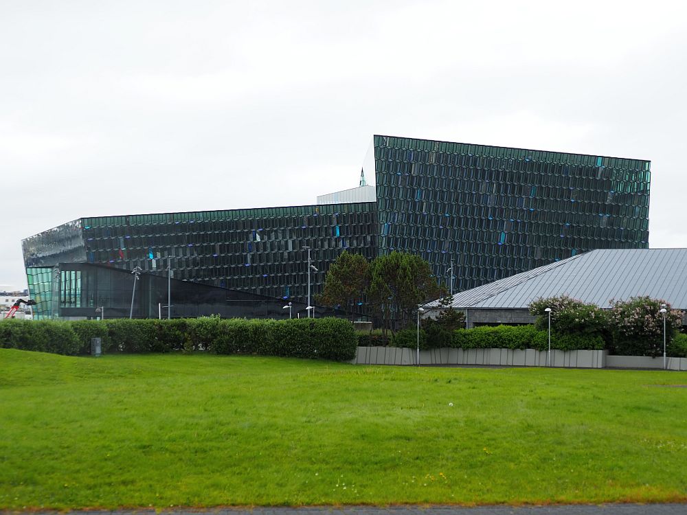 The building is all angles, completely covered in glass panes, looking opaque from this angle on gray day.