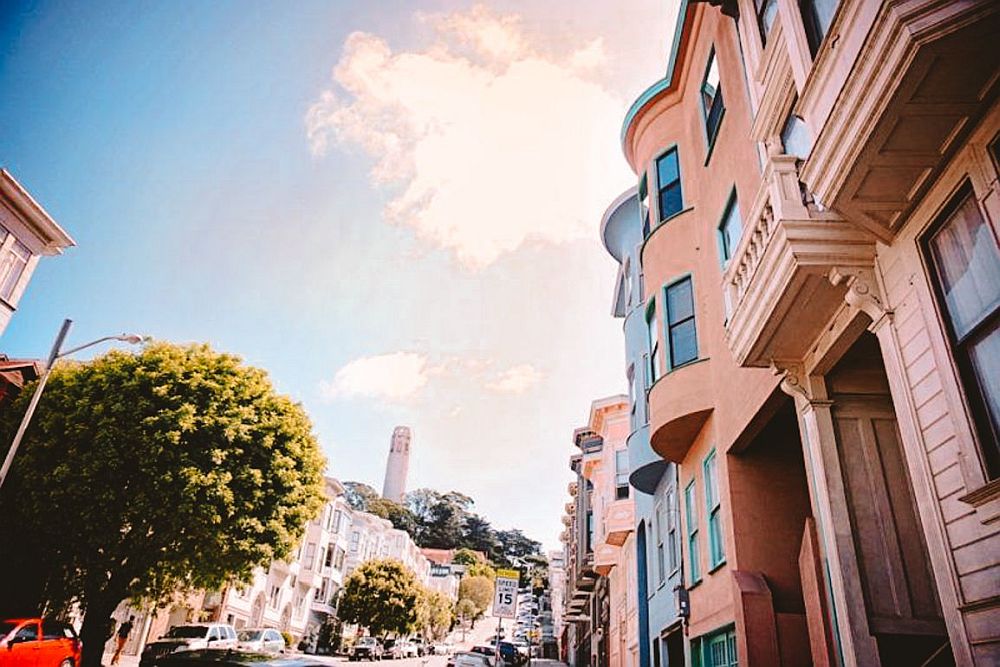 A view up the hill toward Coit Tower, which is visible in the distance. Houses line both sides of the road up the hill.