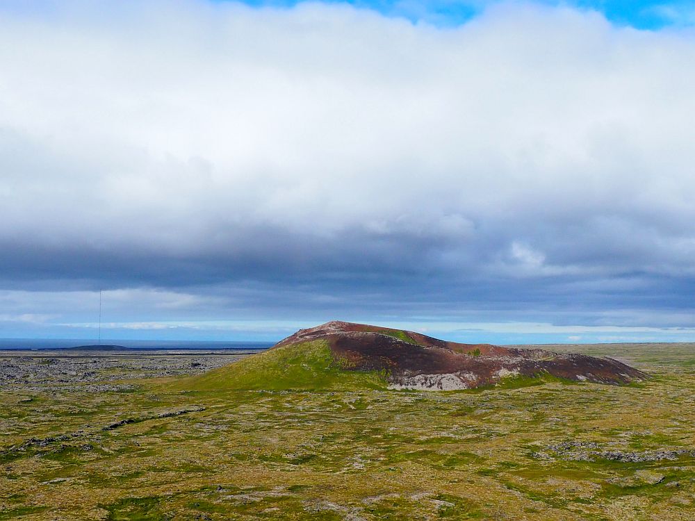 A flat, grass covered view for a long distance, except for a collapsed crater in the middle distance.