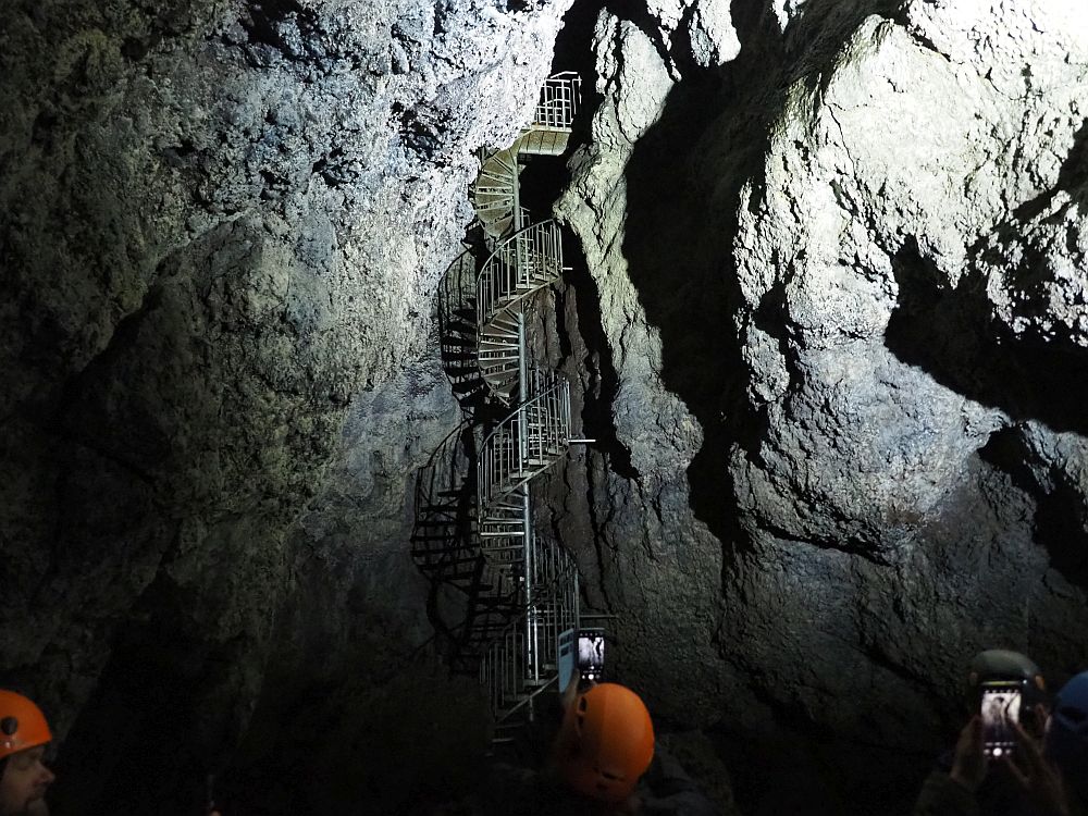 In a wall of rock ,a metal spiral stairway rises up through an opening.