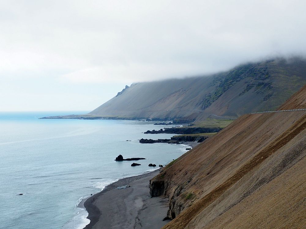 A view along the coast. The hills on the right descend steeply down to the sea. The tops of the hills are obscured by a flat-bottomed layer of cloud.