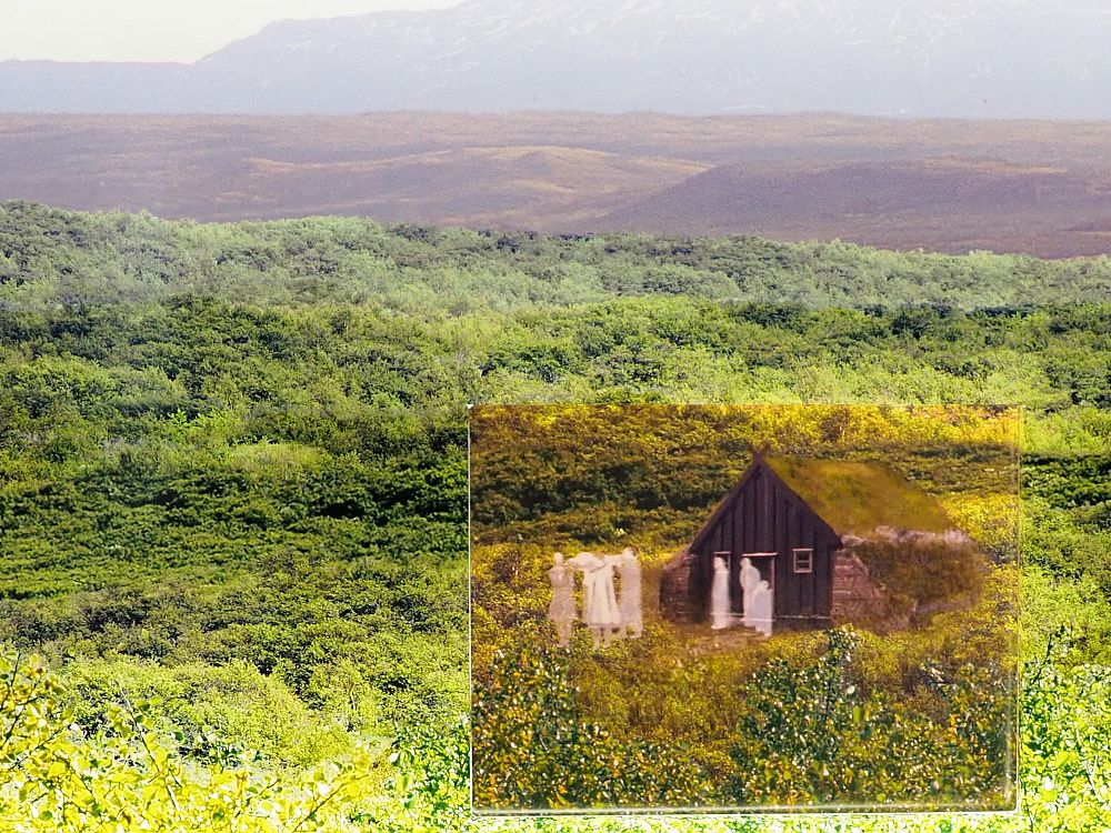 The projection shows a green field with browner fields in the distance. In the foreground an image is superimposed on the green background. It shows a small brown house with a turf roof and white, ghostly figures in robes coming out of the door, carrying what looks to be a coffin.