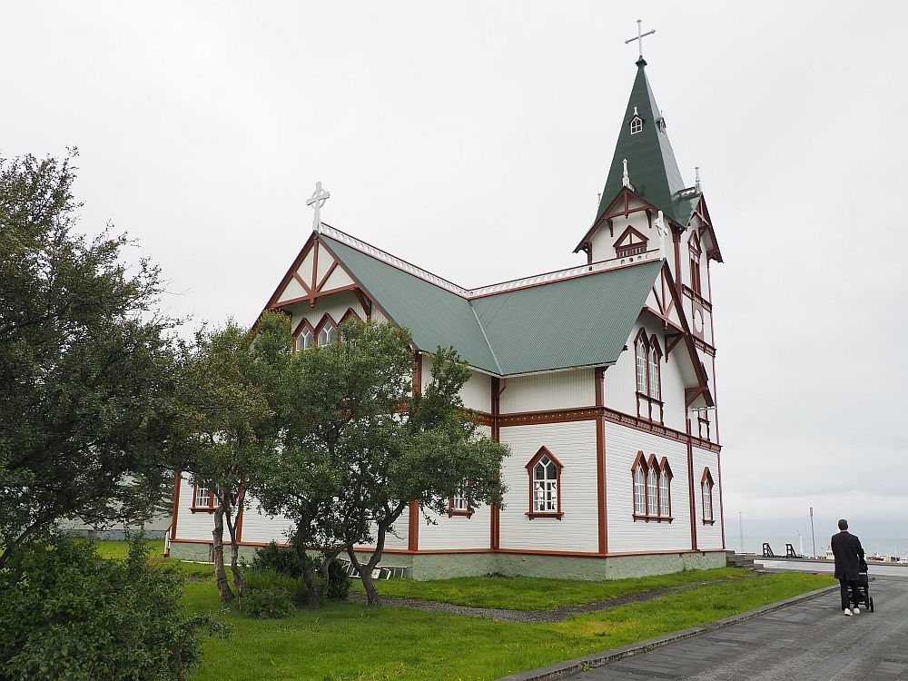 More ornate and bigger than most churches in Iceland, the building is cross-shaped and two storeys tall. The steeple is three stories tall and only narrows at the roof level. The walls are white but the window frames and other edge details are in a brownish-red. 