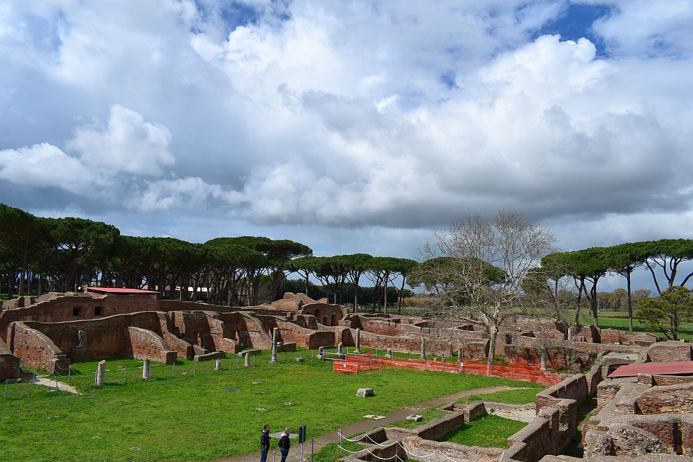 A complex of stone walls surrounds three sides of a grassy open area. It seems that there were many small rooms, built with some sort of reddish stone or brick.