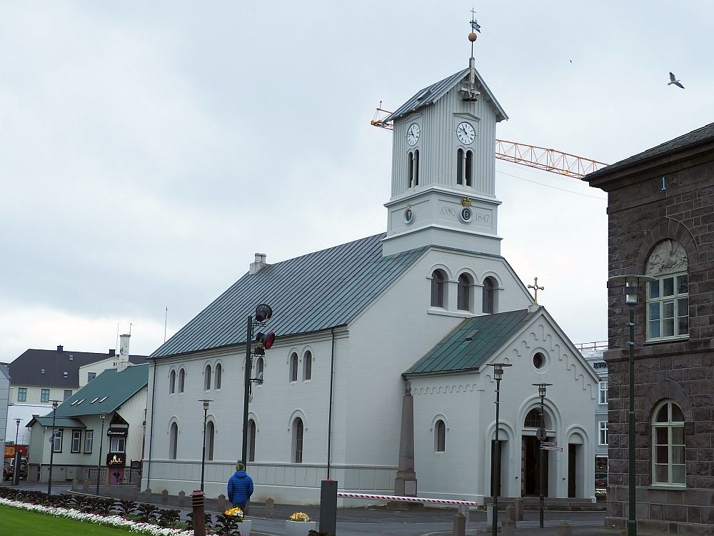 The church is white and a simple design: a peaked roof down the center and a square short tower at one end. The entrance extends outward and is smaller, so the peak of its roof is lower. 