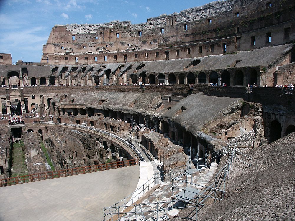 The curve of one side of the colosseum has slanted levels where seats would have onece been, and the crumbling outer wall of the colosseum beside that.