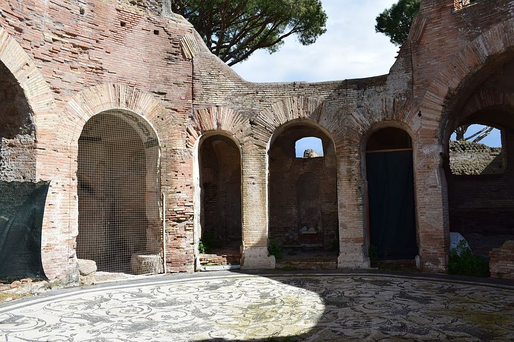 Arches surround the room in curve, open to the sky. The arches are made of brick rather than stone. The round floor is covered in a mozaic that is just grey and white and has a number of figures of animals.