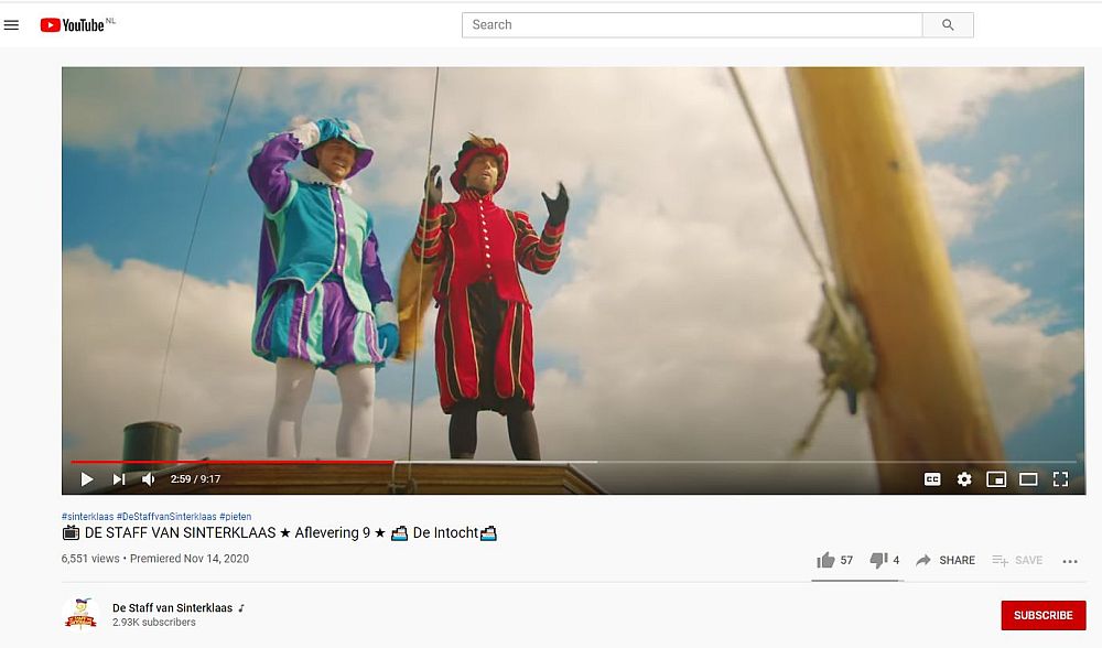 Two Petes stand on a boat (Sinterklaas's steamboat, I think) looking into the distance. They both wear bright outfits: on the left it's turquoise and purple, on the right it's red and brown. Both have snug jackets with puffy sleeves and puffy shorts to above the knee. Both wear tights under that. Neither has a sooty face; they're both white-skinned.