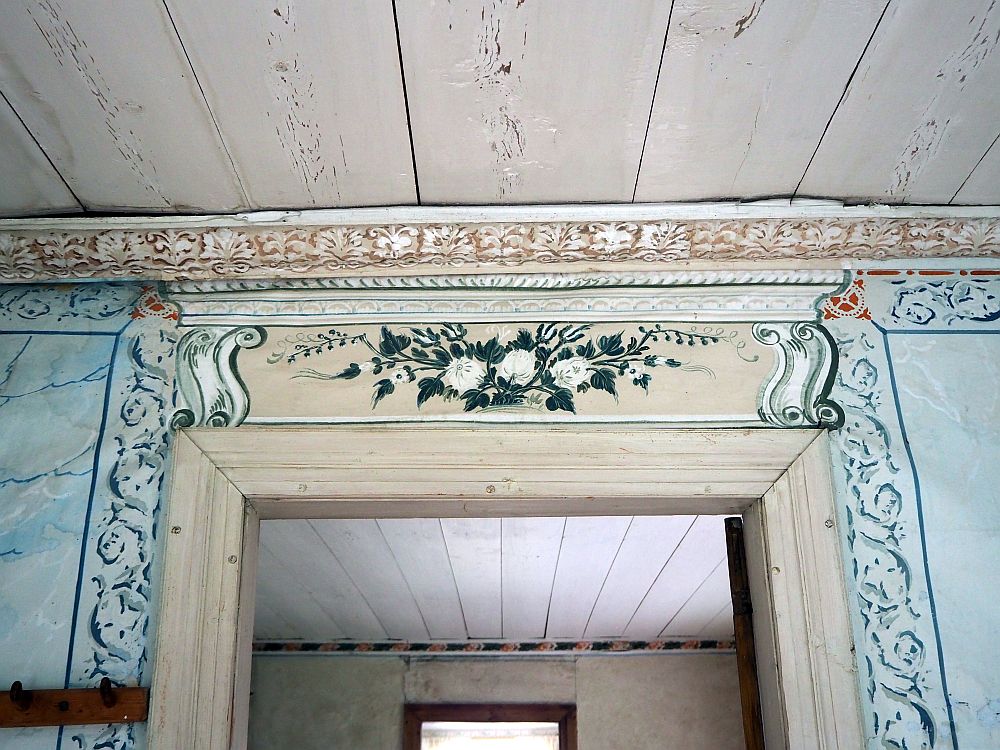 Above the door is a painted set of 3 flowers in white on dark green leaves. Beside the door are some scrolly shapes that I think are intended to be trompe l'oeil carvings. 