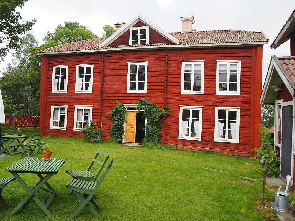 The house is red-painted wood. The door sits right in the middle with two windows on either side of it. Upstairs is one more story: one window in the center above the door and two windows on either side. 