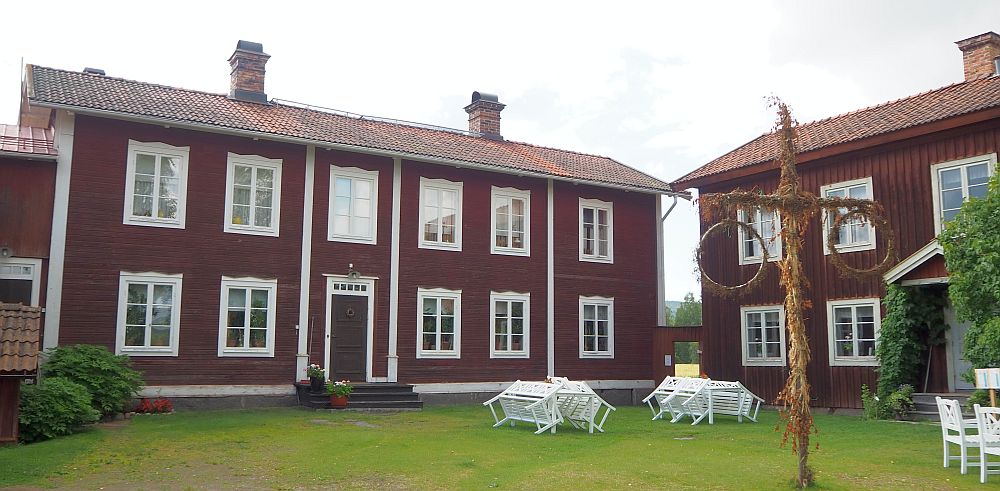 The house is dark red with white edging. The photo shows the center house and only part of the right-hand side house. The central house is not symmetrical: The door has 2 windows to the left of it and 3 to the right. The house has two stories.