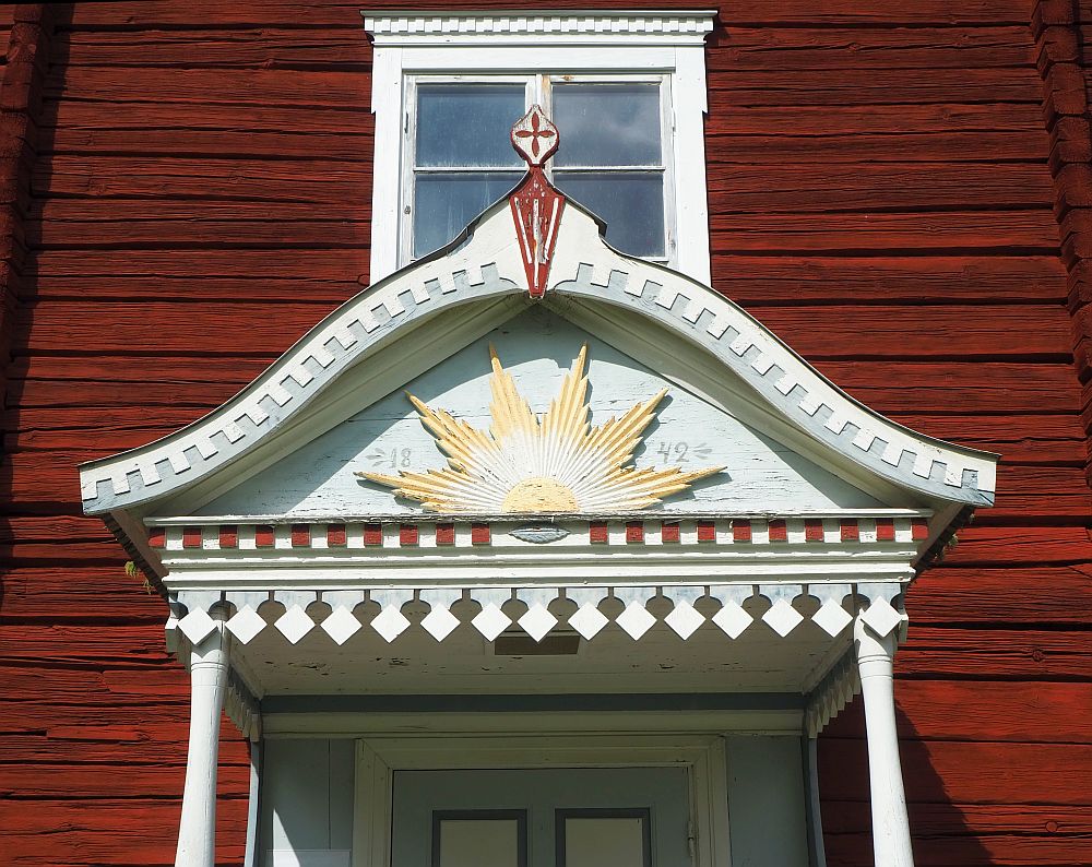 The roof over the front door is carved with a edge of pointy teeth. Above that is a half of a sun in the center of the little roof.