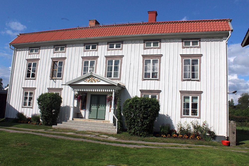 A large white house with three stories. The door sits symmetrically in the center with a large portico roof over the steps up. Two windows on either side of the central door. 6 windows on the story above that. 6 more windows (but much smaller) above that, under the roof.