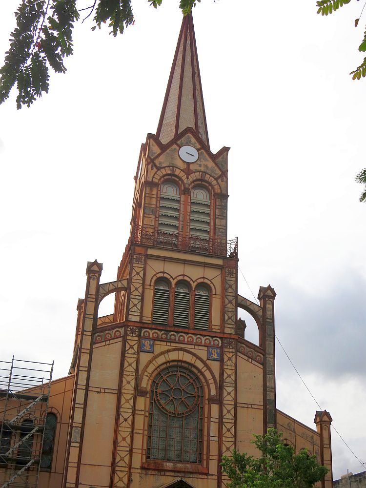 The tower is tiered, so the lower parts are bigger than the upper ones. Itis a light brown color with reddish brown along all of the edges and around the arched window bottom center. A flying buttress supports the tower where it stands on the roof of the church.