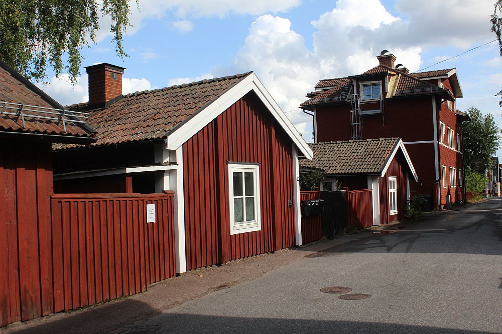 A row of red-painted houses. The nearer ones are very small and just one story. The furthest one is 3 stories tall. 