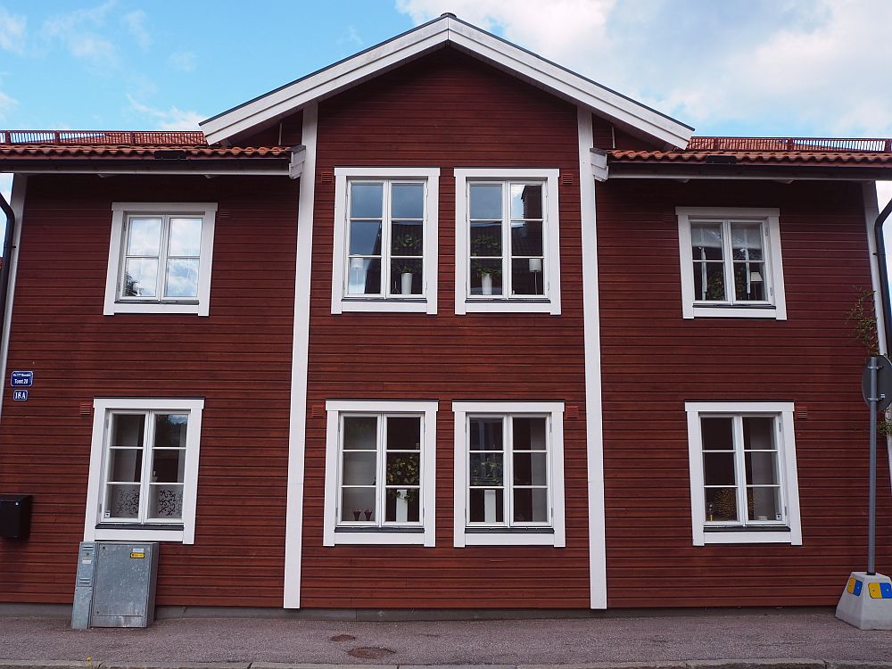 The house is 2 stries high, painted deep red with white around the windows and roof, and two white strips down around the central two windows. Four windows on each of 2 floors. 