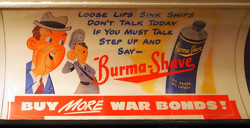 Ad has a cartoonish drawing of a businessman (jacket and tie and hat) and Hitler (uniform and cap with swastikas). The businessman looks like he's whispering to Hitler. On the right is a drawing of a bottle of Burma Shave that says "no brush no lather". Between the two drawings are the words "Loose lips sink ships Don't talk today if you must talk step up and say -- Burma-Shave". Across the bottom are the words "Buy more war bonds!"