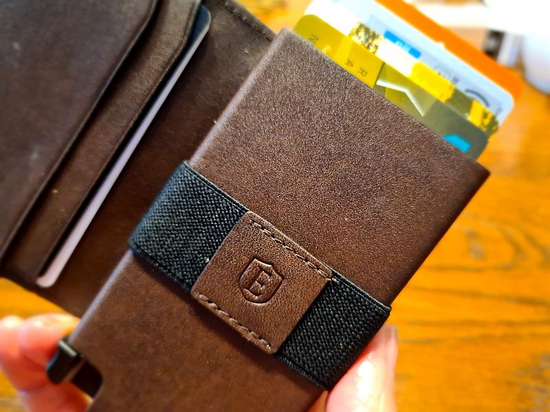 The wallet is open in this photo, and the knob on the lower left is visible, with a person's finger pushing it. At the top of the wallet, the tops of 4 cards peek out, each a bit further out than the one in front of it so all 4 are visible.