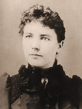 a black-and-white photo of Laura Ingalls Wilder: hair pulled back, short-cut bangs, eyes looking off to the left a bit, Black high collar.