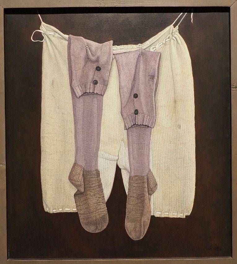 The painting shows long white woolen knitted underwear hanging on a wall and two long pink knitted socks hanging from the underwear. The detail is almost photographic, showing the weave of the knitting.