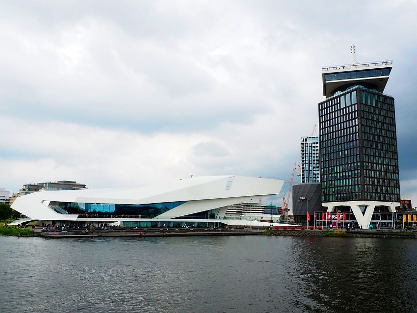 The Eye Museum is a low and white modern building with dramatic curves. Next to it is a tower with the top several stories set at an angle to the rest.