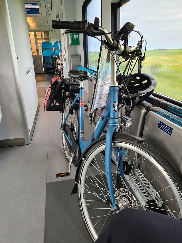 The bicycle leans against a window, where a flat green field is visible. A helmet hangs from the handlebar.