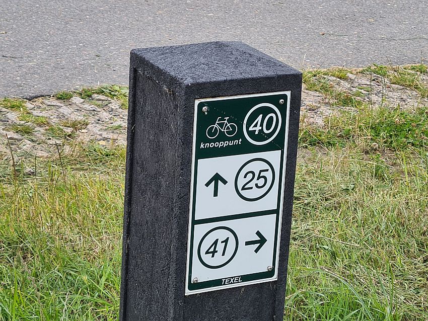 A short wooden pole with a sign attached to it. At the top, a line drawing of a bicycle next to the number 40 in a circle. Below, the numbers 25 and 41, each in a circle with an arrow next to it.