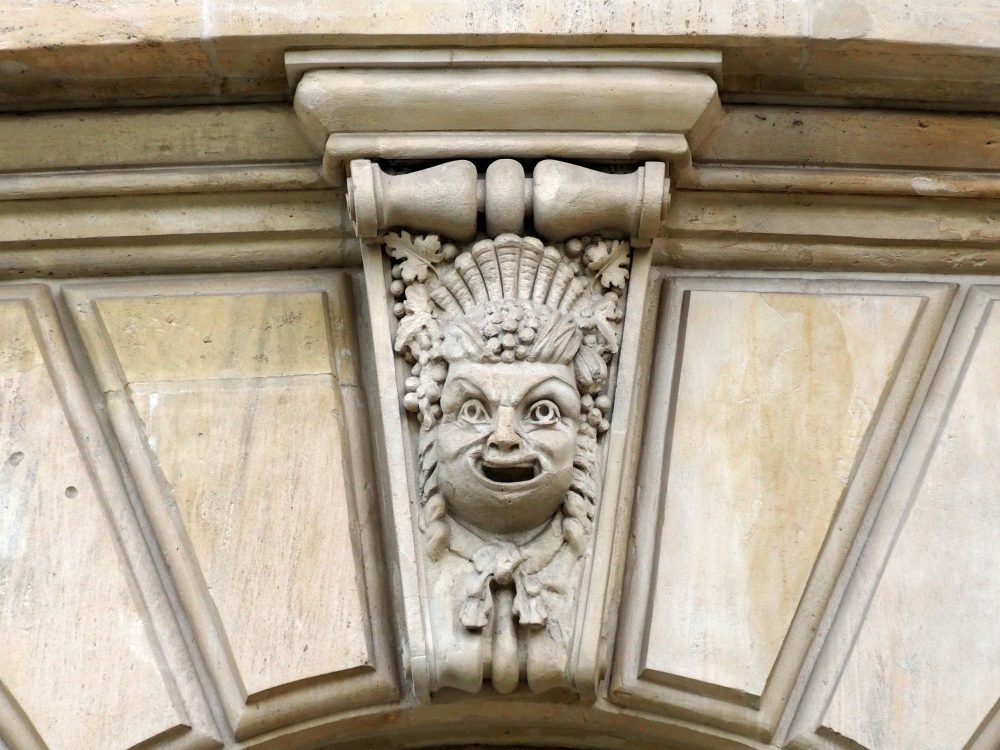 A face smiles comically, wearing an odd headress and curls down the sides.