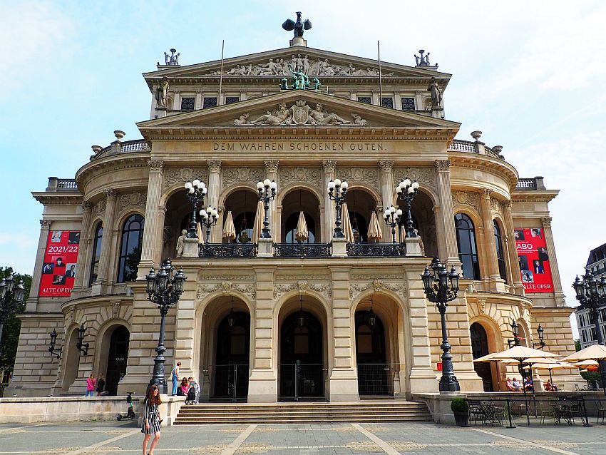 A classical design with 3 arched entryways on the ground floor, pillars above that holding up a pediment that reads Dem Wahren Schoenen Guten. In the triangle of the pediment, two reclining figures framing a coat of arms. Above that, a statue on the peak of the pediment and both corners. Above that, another story with yet another pediment, with a large and detailed bas-relief inside it and again, statues on the corners and peak.