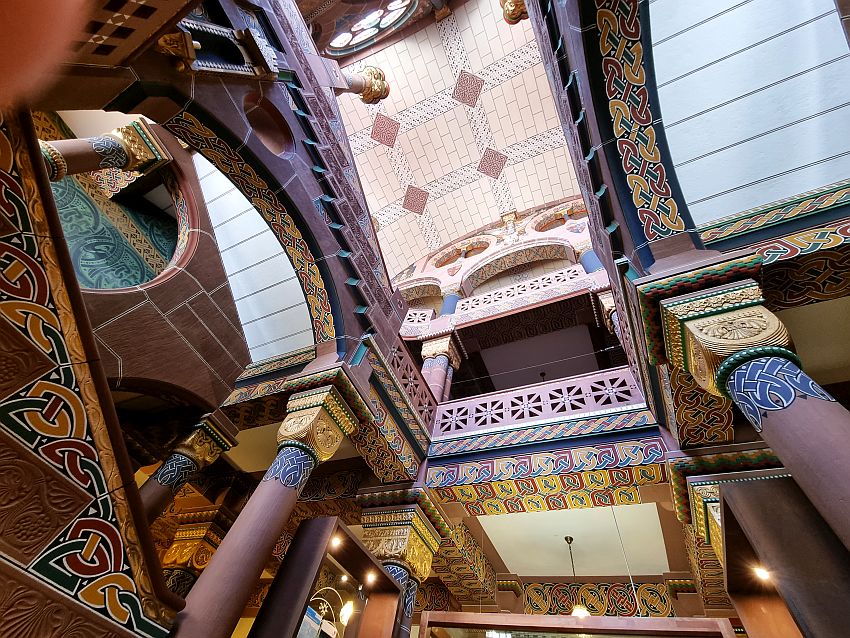 Intricate patterns painted on the arched ceiling and the pillars holding it up. To the left of the picture a bit of a painted wall is visible over a painted railing of stairway up. Hart to describe because it's all so intricate and complex in this view.