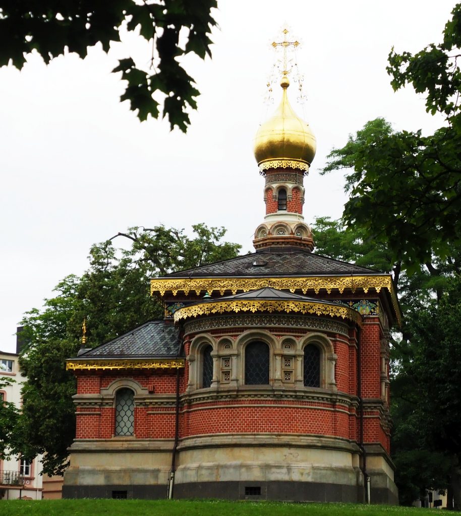 The church is made of red brick and has a rounded section in front that I assume is the altar. It's a very small building and the small steeple is round, with an onion dome on top. The dome is gold as is a filigreed edging around the roof lines below.