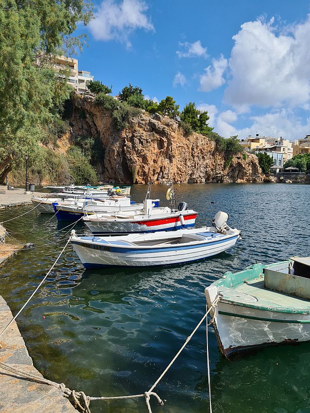 The boats are very small, like rowboats, except with a small outboard motor at the back of each. They are tied with ropes to the dock that runs along the water. Beyond them is a cliff.