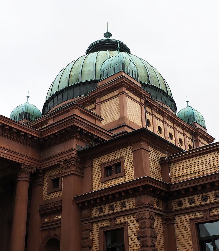 The walls are a yellowish brick with dark red stone edges and columns. The domes above are green copper: one large central dome and 3 smaller ones visible in this photo.