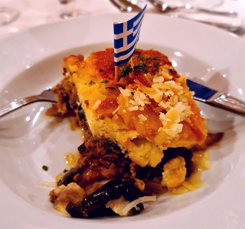 A square of moussaka with a little blue and white Greek flag on a toothpick in the middle.