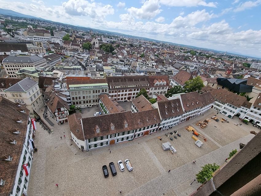 Looking down on Munsterplatz, the open square around the cathedral. It is lined with neat buildings of 3-4 stories. All are painted white and have neat rows of windows on each floor, with shutters open. Beyond the  Munsterplatz the view looks over the roofs of the city, all quite low on this side of the city.